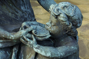 A bronze statue of a toddler being fed from a bowl.