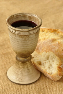 A brown stone cup of wine and some slices of bread on a burlap covered table