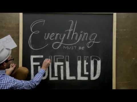 Man writing on a chalk board that everything must be fulfilled.